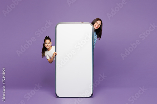 Full body young woman child baby girl 8-9 years old wear blue casual clothes. Mommy little kid behind big huge blank screen mobile cell phone isolated on plain purple background Mother's Day concept.