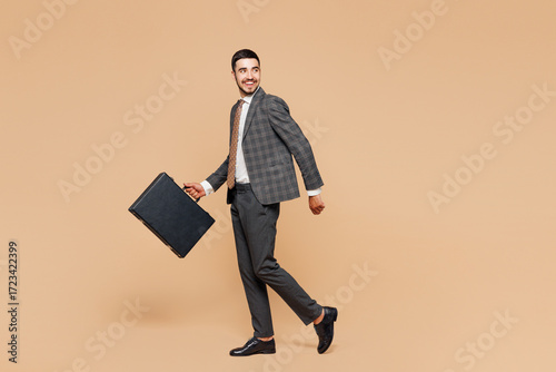 Fotografia Full body side view young employee business man corporate lawyer wear classic formal grey suit shirt work in office hold in hand black briefcase look aside isolated on plain beige background studio