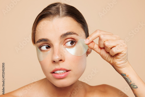 Bilde på lerret Beautiful half naked topless young woman 20s with nude make up wearing patch under eye isolated on plain beige color wall background studio portrait