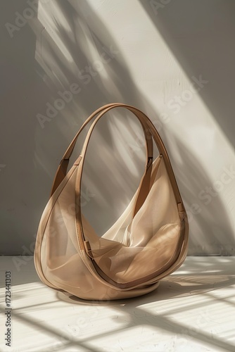 A pale beige, semi-sheer tote bag with tan leather handles rests on a light surface, illuminated by soft, dappled sunlight