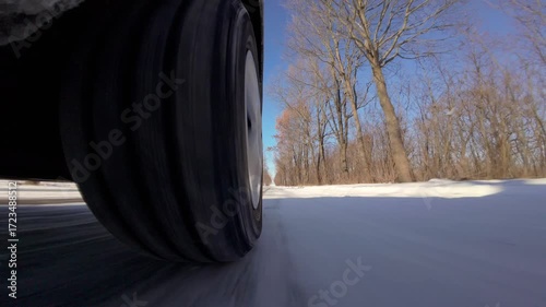 A car wheel drives on a snowy road on a winter day. Close-up video of a car tire driving on a road covered in snow and ice on a sunny winter day