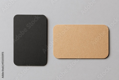 Two blank business cards, one black and one light beige, lie on a neutral gray surface