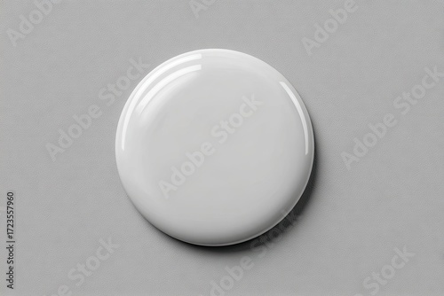 High-angle close-up of a perfectly round, glossy, white liquid droplet or paint blob on a neutral gray surface
