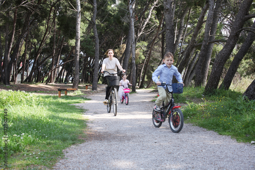 Obraz premium mother with children riding a bike in green park, lifestyle people concept