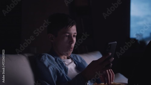 Quiet Evening: Boy Enjoying Solitude by the Window, Snacking on Chips and Using His Phone