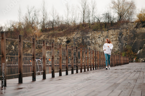 Smiling red-haired girl in white hoodie with headphones on her head running