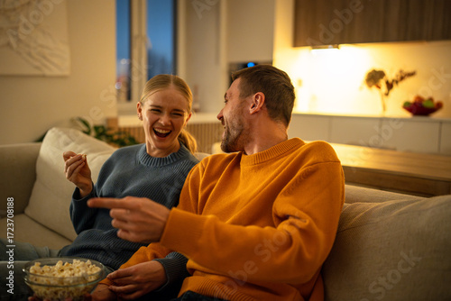 Obraz na plátně Couple laughing to tears while watching movie and joking on sofa during Friday evening at home