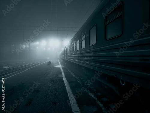 Night, fog, railway station, passenger train is at the station, platform and carriages are illuminated by floodlights, black and white photo