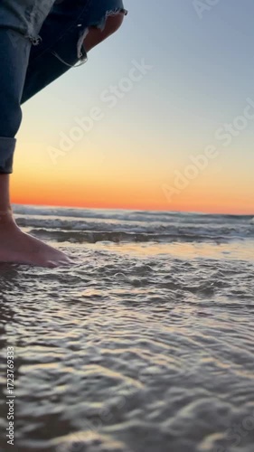 slow-motion video of bare feet walking through the sea along the beach at sunset. Water splashes gracefully with each step