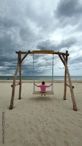 joyful woman is sitting on wooden swing on the beach, happiness and cheerfulness in autumn	
