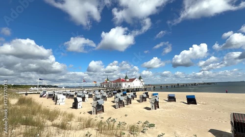 traditional wicker beach chairs (Strandkörbe) set on golden sand by the sea, under a vivid blue sky with fluffy white clouds, evoking a serene, coastal vibe