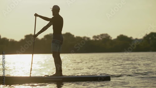Active man paddle boarding on lake surrounded by nature	