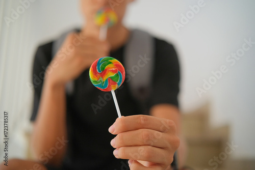 Teenager with backpack sitting on stairs and offering one lollipop while eating another