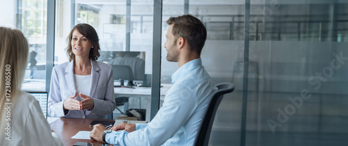 Team of young European man and Latin businesswoman discussing project sitting at table in office. Business people work together. Female woman mentor leader coach have meeting. Banner, copy space