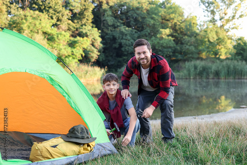 Bilde på lerret Happy father and son setting up camping tent near river outdoors