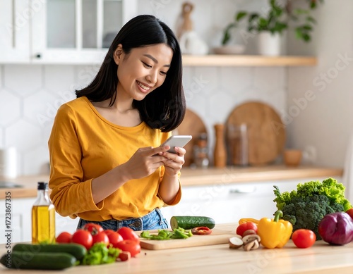 Woman in kitchen using phone, fresh vegetables