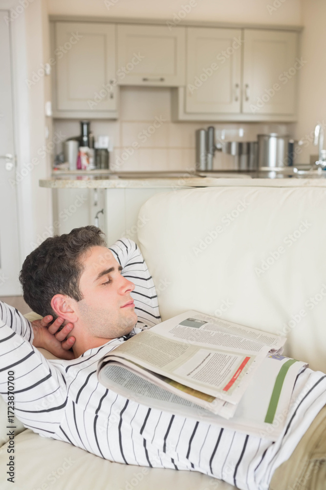 Obraz premium Male reclining on white leather couch, dozing in open-plan living area with newspaper and kettle