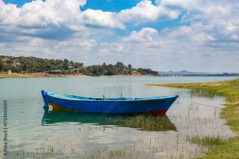 Obraz premium A peaceful lakeshore view. Nature landscape with empty fishing boat standing on the shore.