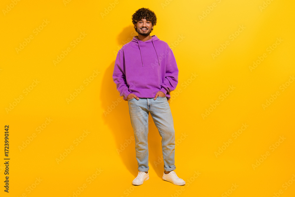 Fototapeta premium Young man wearing a vibrant purple hoodie, posing with a confident smile against a bright yellow background.