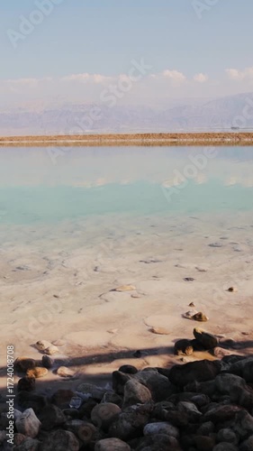 View of the sea beach at daytime. Mountains are far away. Dead sea near Ein Bokek, Israel. Shore of the Dead Sea in calm weather. Vertical video