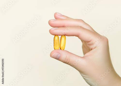 Hand holding two yellow vitamin capsules