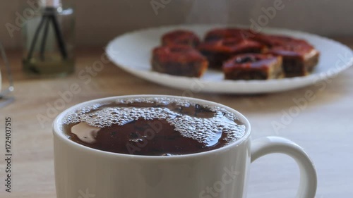 Freshly brewed tea is stirred in a cup on the table with a spoon. Medium shot.