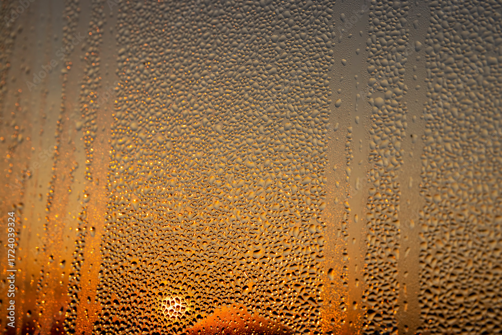 Obraz premium water droplets from condensation on the window glass at sunset, wet glass with lots of water droplets on the background of an orange sky