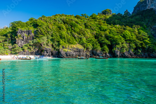 Nui Beach in Krabi, Thailand, featuring a small sandy beach nestled against lush green cliffs with longtail boats floating on clear turquoise water and people enjoying the tropical scenery