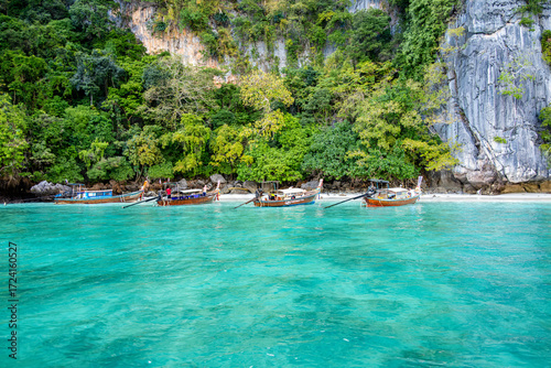Four traditional thai longtail boats are resting in the calm turquoise water of Monkey Bay. With lush vegetation and limestone cliffs in the background. Located in Phi Phi Don Island. Krabi. Thailand