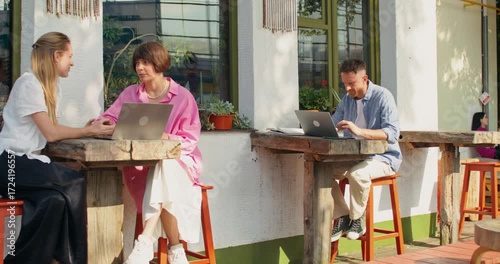 Two women are discussing a joint project on a laptop while sitting on a cafe terrace.