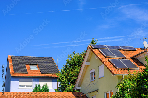 Wohnhäuser mit Solaranlagen zur Erzeugung von Strom und Warmwasser auf roten Hausdächern vor blauem Himmel