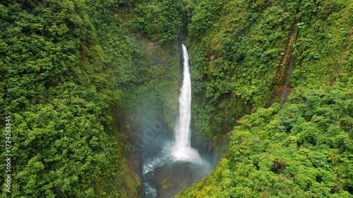 Tall waterfall cascades into rocky pool surrounded by lush green rainforest