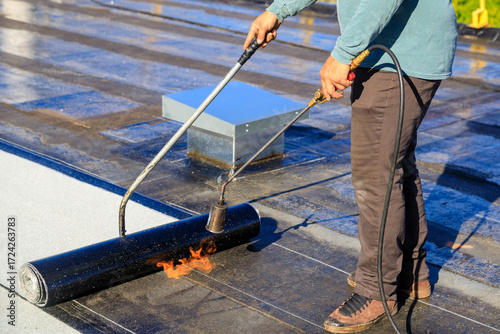 Roofer applying torch to bitumen membrane on torch down roof