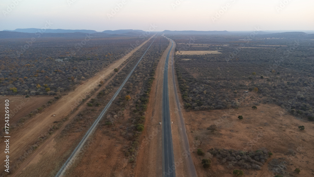 Naklejka premium A long straight road cutting through a dry, rural landscape from above