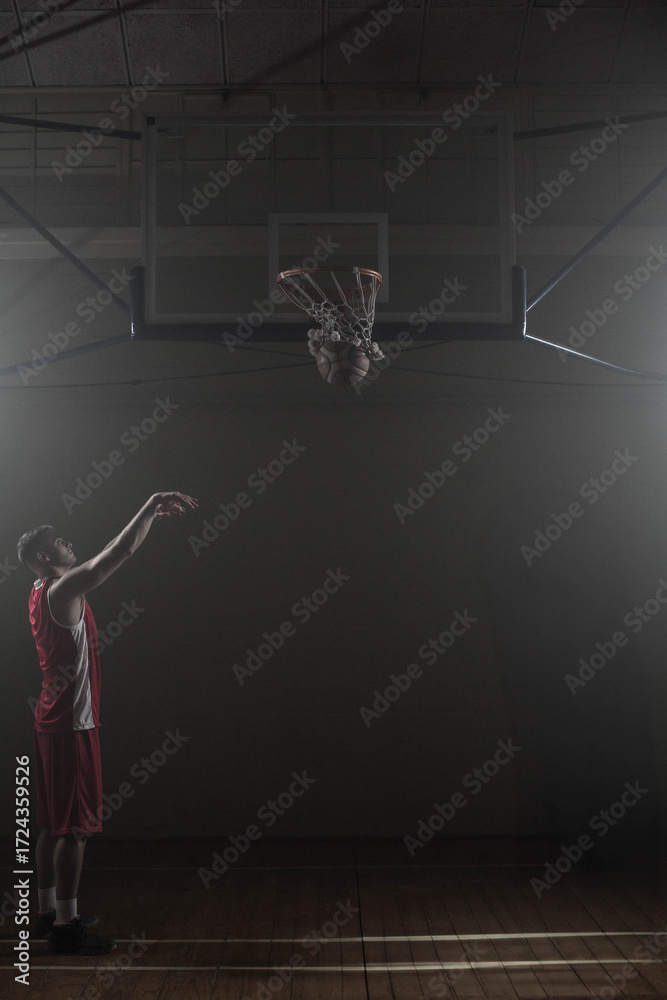 Fototapeta premium Basketball falling through net on wooden gym court under spotlights with deep shadows