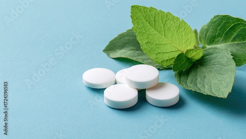 White pills beside fresh mint leaves on a light blue surface