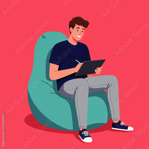 A young man sits comfortably in a beanbag chair, drawing or writing on a digital tablet with a stylus.