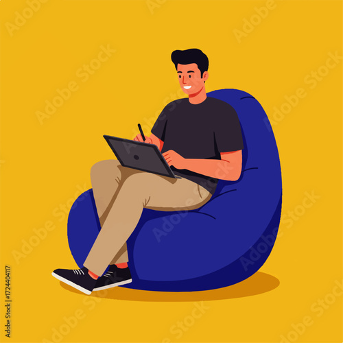A young man sits comfortably in a blue beanbag chair, smiling and working on a laptop with a stylus.