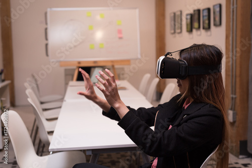 Asian woman immersing in VR world at office meeting table wearing headset, copy space