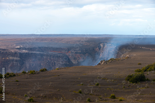 Halemaʻumaʻu Crater in Hawaiʻi Volcanoes National Park, Big Island, Hawaii, with volcanic cliffs, smoke, and barren lava terrain.