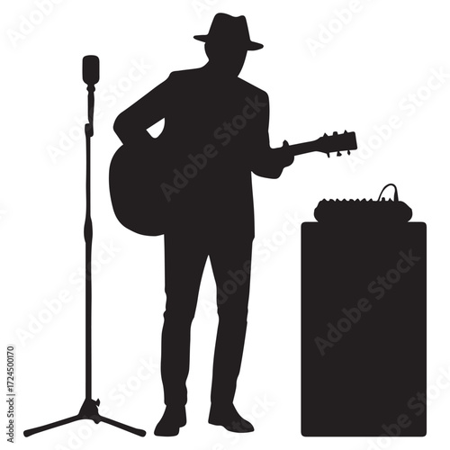 Silhouette of a musician playing guitar and singing on stage. Man wearing a hat standing beside a microphone and sound equipment.