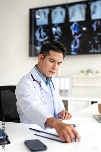 Serious  doctor  working in office,  reading medical document, focused senior therapist physician  wearing doctor gown sitting at desk in hospital, analyzing patient diagnosis or report.