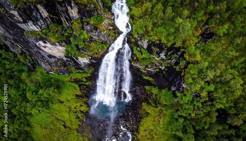 Waterfall cascading down rocky cliff face, surrounded by lush green forest