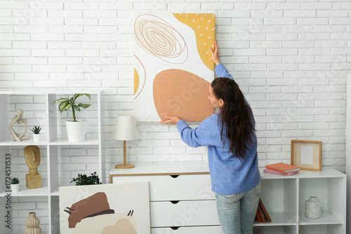 Young woman hanging picture...