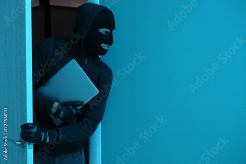 Male thief with stolen laptop walking through door at night