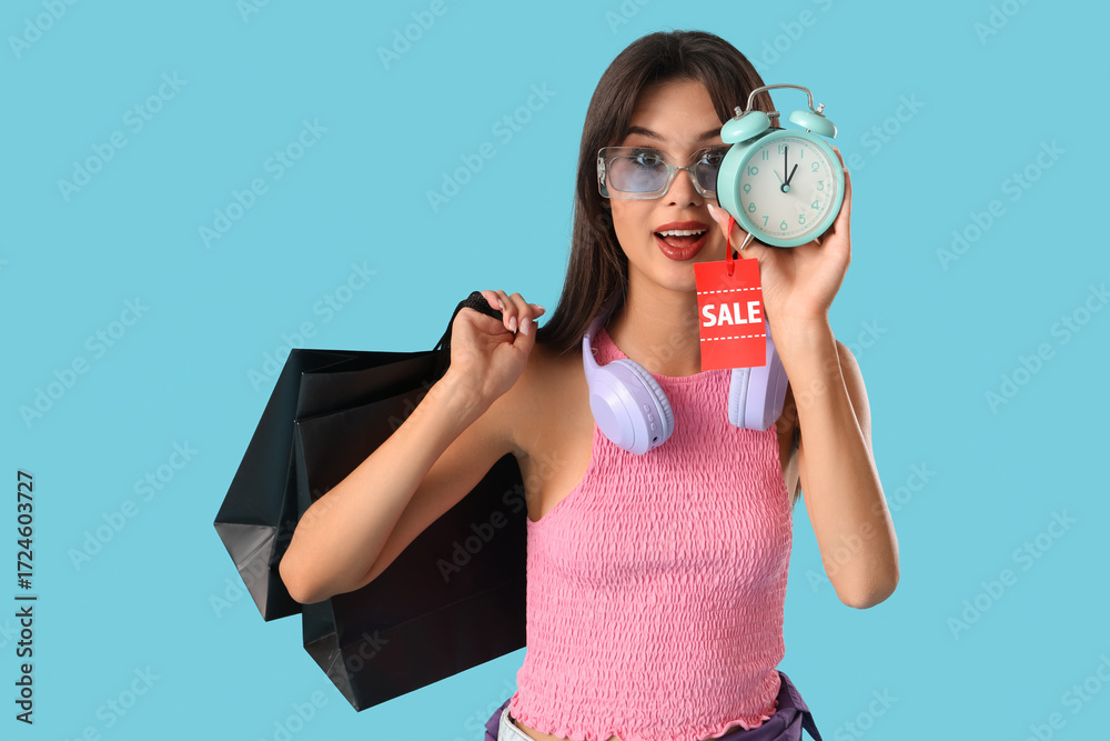 Obraz premium Young woman with shopping bags and alarm clock on blue background. Cyber Monday