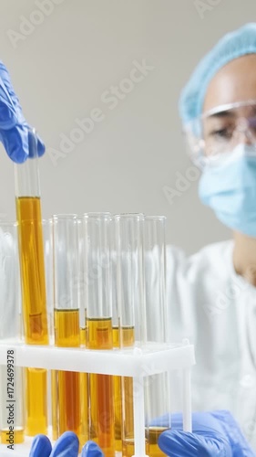 Scientist in lab coat and gloves examines golden oil in test tubes, pouring and analyzing samples.
