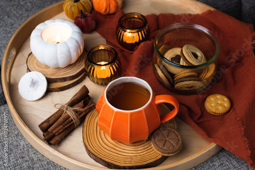 A cozy autumn scene with a tray on a sofa featuring a pumpkin-shaped mug of coffee, cookies in a glass jar, and decorative candles. Warm pillows and a blanket create a relaxed seasonal atmosphere.