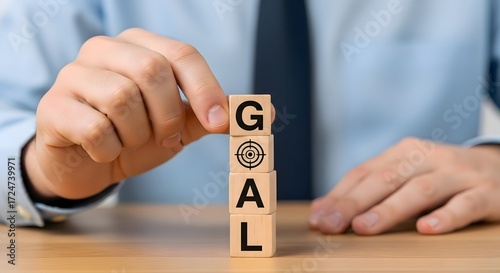 A person stacking wooden blocks spelling goal with a target symbol on a wooden surface table