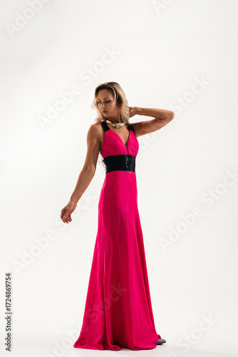 Woman posing in a vibrant pink gown with black accents against a simple backdrop